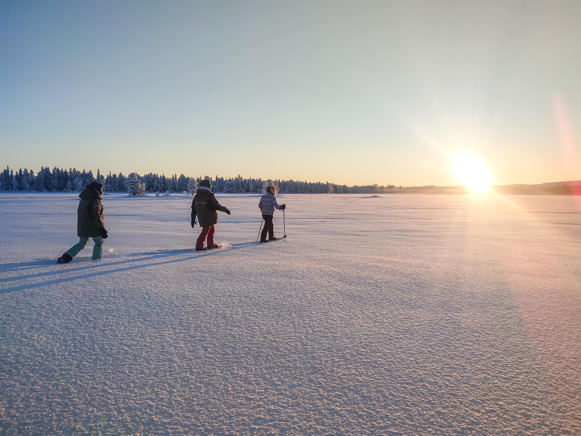 Trois personnes ski durant un coucher du soleil en Laponie